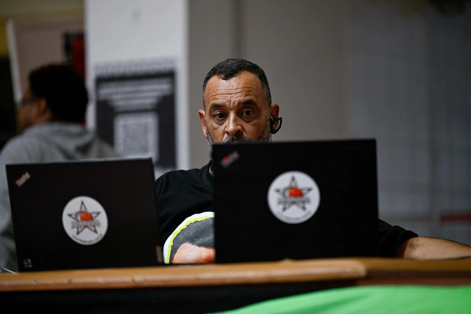 Profissional com headset operando dois computadores nos bastidores da transmissão